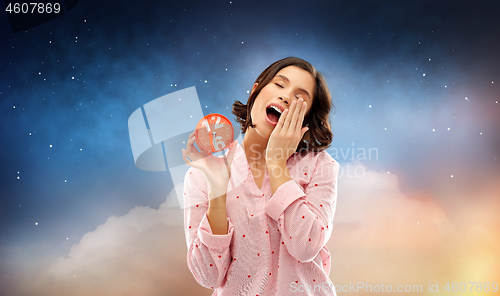 Image of sleepy woman in pajama with alarm clock yawning