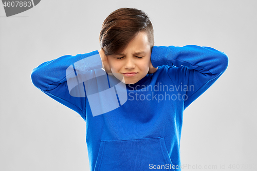 Image of stressed boy in blue sweater closing ears by hands