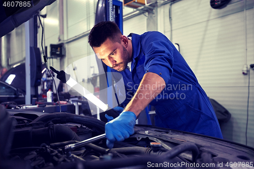 Image of mechanic man with lamp repairing car at workshop