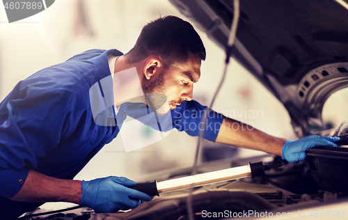 Image of mechanic man with lamp repairing car at workshop