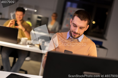 Image of man with smartphone working late at night office