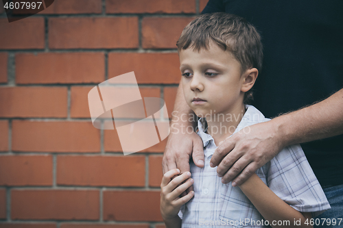 Image of Portrait of young sad little boy and father standing outdoors at