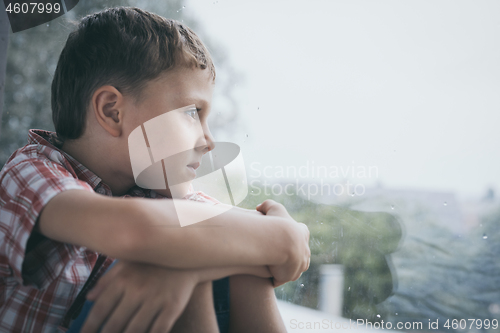 Image of portrait one sad little boy sitting near a window