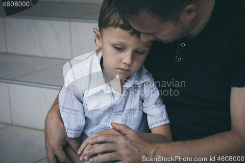 Image of Portrait of young sad little boy and father sitting outdoors at 