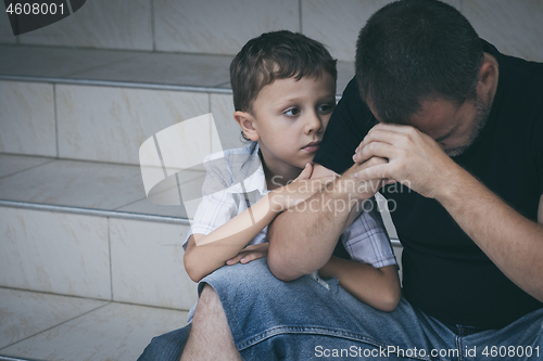 Image of Portrait of young sad little boy and father sitting outdoors at 