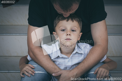 Image of Portrait of young sad little boy and father sitting outdoors at 