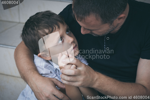 Image of Portrait of young sad little boy and father sitting outdoors at 