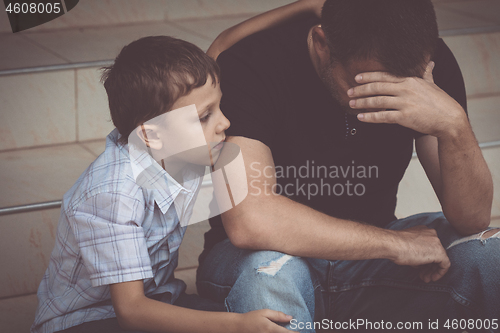 Image of Portrait of young sad little boy and father sitting outdoors at 