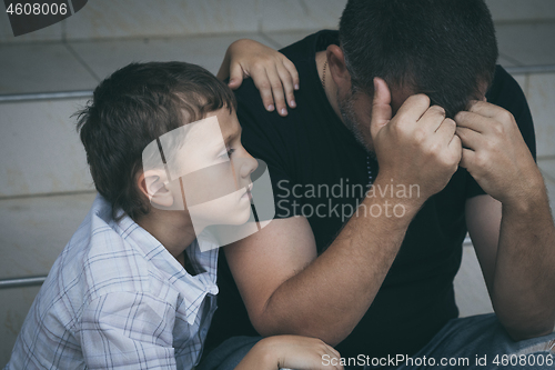 Image of Portrait of young sad little boy and father sitting outdoors at 