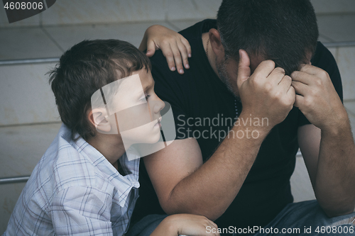 Image of Portrait of young sad little boy and father sitting outdoors at 