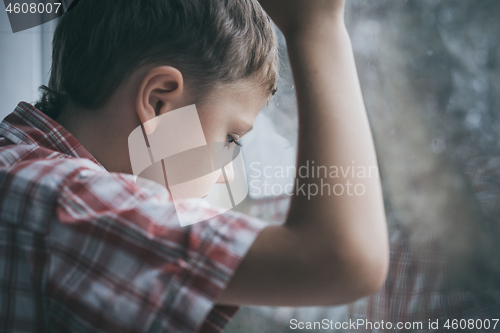 Image of portrait one sad little boy sitting near a window