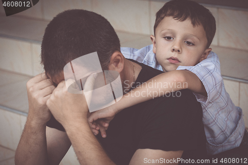 Image of Portrait of young sad little boy and father sitting outdoors at 