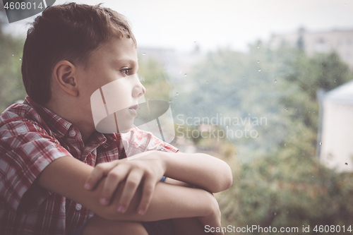 Image of portrait one sad little boy sitting near a window