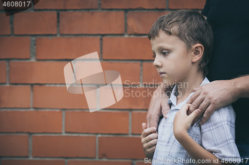 Image of Portrait of young sad little boy and father standing outdoors at