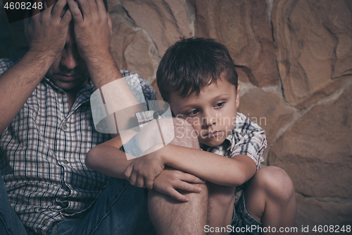 Image of Portrait of young sad little boy and father sitting outdoors at 