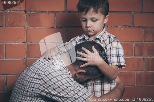 Image of Portrait of young sad little boy and father sitting outdoors at 