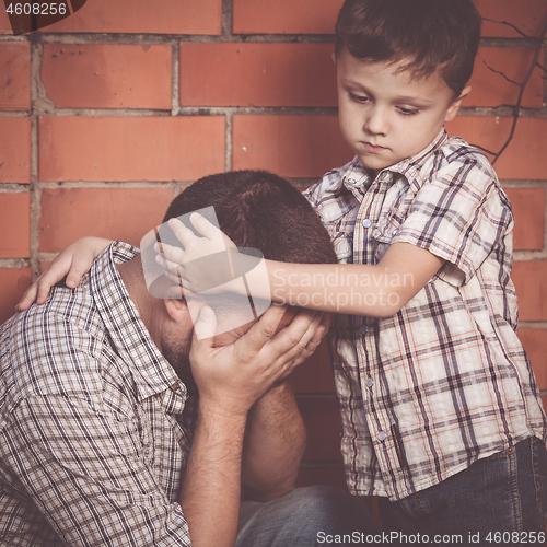 Image of Portrait of young sad little boy and father sitting outdoors at 