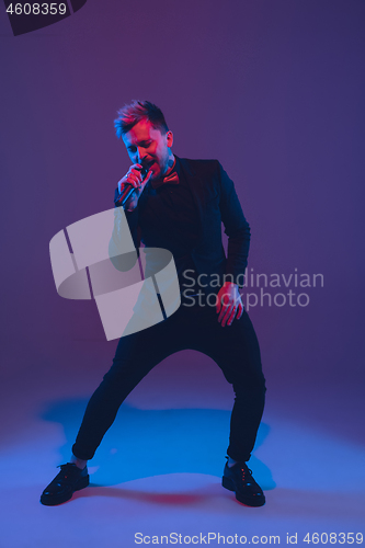 Image of Young caucasian musician, performer singing, dancing in neon light on gradient background