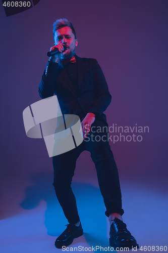 Image of Young caucasian musician, performer singing, dancing in neon light on gradient background