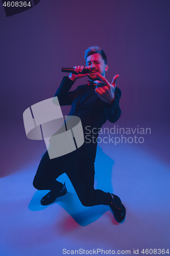 Image of Young caucasian musician, performer singing, dancing in neon light on gradient background