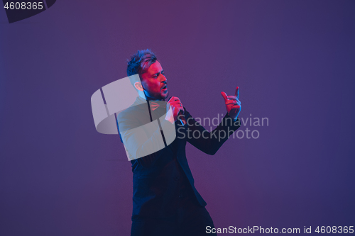 Image of Young caucasian musician, performer singing, dancing in neon light on gradient background