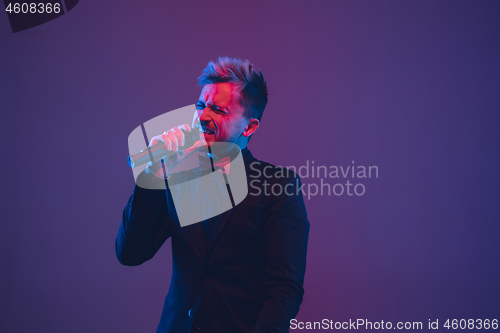 Image of Young caucasian musician, performer singing, dancing in neon light on gradient background