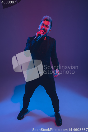 Image of Young caucasian musician, performer singing, dancing in neon light on gradient background