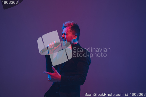 Image of Young caucasian musician, performer singing, dancing in neon light on gradient background