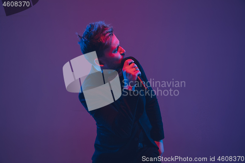 Image of Young caucasian musician, performer singing, dancing in neon light on gradient background