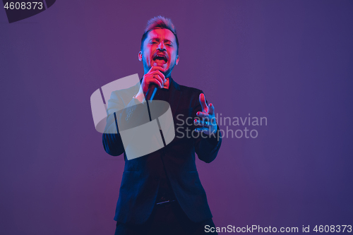 Image of Young caucasian musician, performer singing, dancing in neon light on gradient background