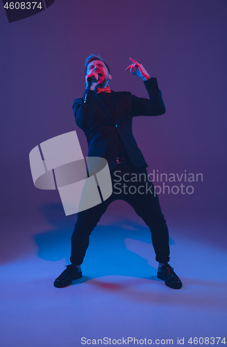 Image of Young caucasian musician, performer singing, dancing in neon light on gradient background