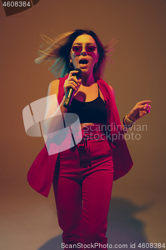 Image of Young caucasian female musician, performer singing, dancing in neon light on gradient background