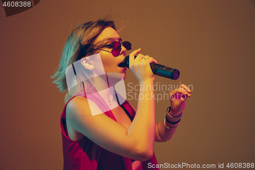 Image of Young caucasian female musician, performer singing, dancing in neon light on gradient background