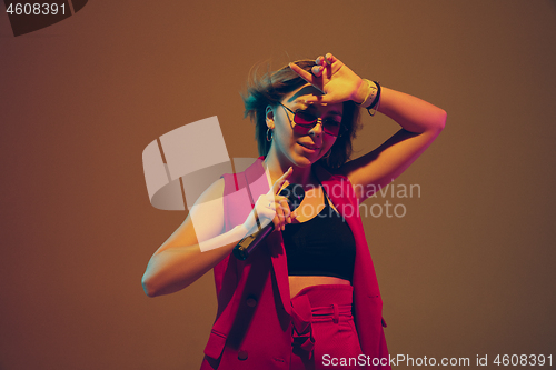 Image of Young caucasian female musician, performer singing, dancing in neon light on gradient background