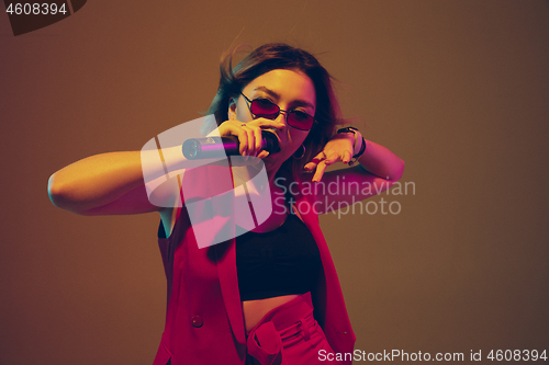 Image of Young caucasian female musician, performer singing, dancing in neon light on gradient background