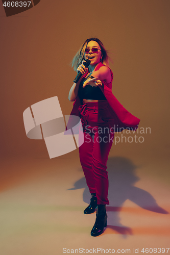 Image of Young caucasian female musician, performer singing, dancing in neon light on gradient background