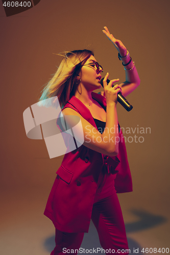 Image of Young caucasian female musician, performer singing, dancing in neon light on gradient background