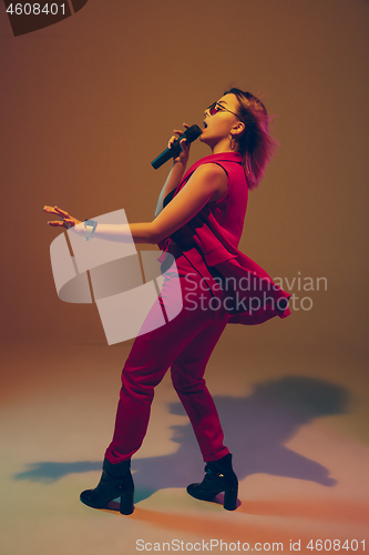 Image of Young caucasian female musician, performer singing, dancing in neon light on gradient background