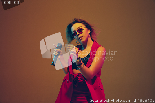 Image of Young caucasian female musician, performer singing, dancing in neon light on gradient background