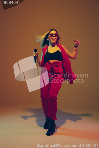 Image of Young caucasian female musician, performer singing, dancing in neon light on gradient background