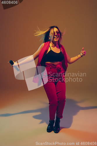 Image of Young caucasian female musician, performer singing, dancing in neon light on gradient background