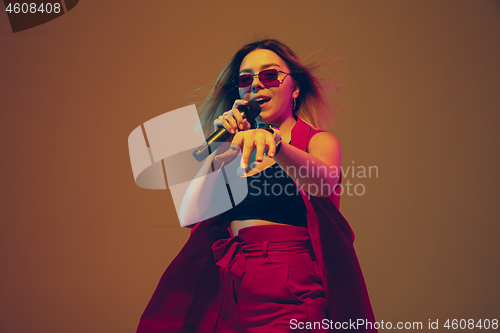 Image of Young caucasian female musician, performer singing, dancing in neon light on gradient background