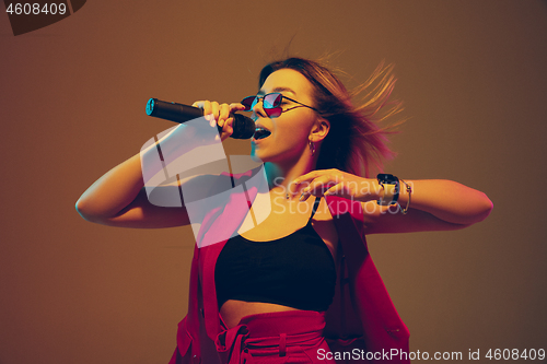 Image of Young caucasian female musician, performer singing, dancing in neon light on gradient background