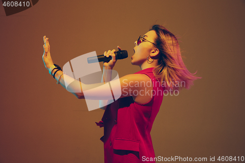 Image of Young caucasian female musician, performer singing, dancing in neon light on gradient background