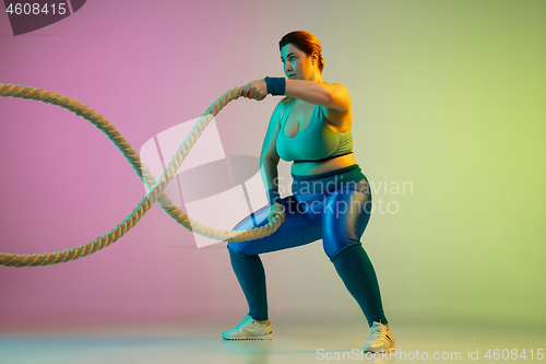 Image of Young caucasian plus size female model\'s training on gradient purple green background