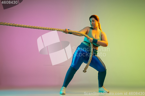 Image of Young caucasian plus size female model\'s training on gradient purple green background
