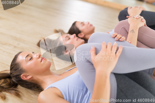 Image of Group of three young sporty attractive women in yoga studio, lying on the floor, stretching and relaxing after the workout. Healthy active lifestyle, working out indoors in gym