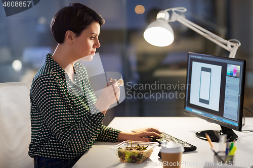 Image of designer eating and working at night office