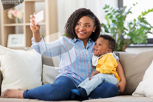 Image of african mother with baby son taking selfie at home