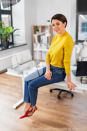 Image of happy businesswoman sitting on desk at office